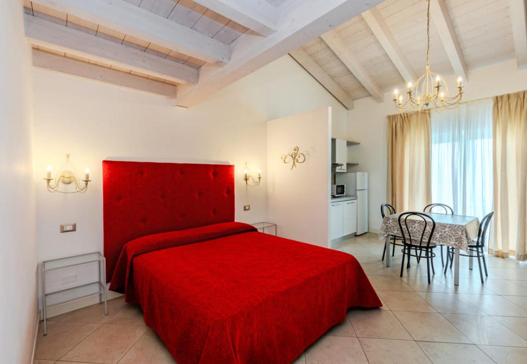 Camera da letto moderna con letto rosso e cucina a vista.
