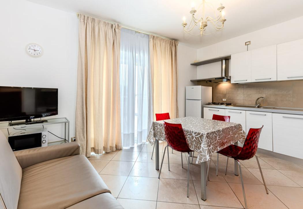Cucina moderna con tavolo, sedie rosse, TV e divano beige.