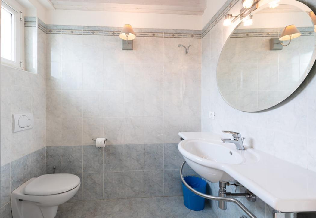Bagno luminoso con specchio ovale, lavandino e WC.