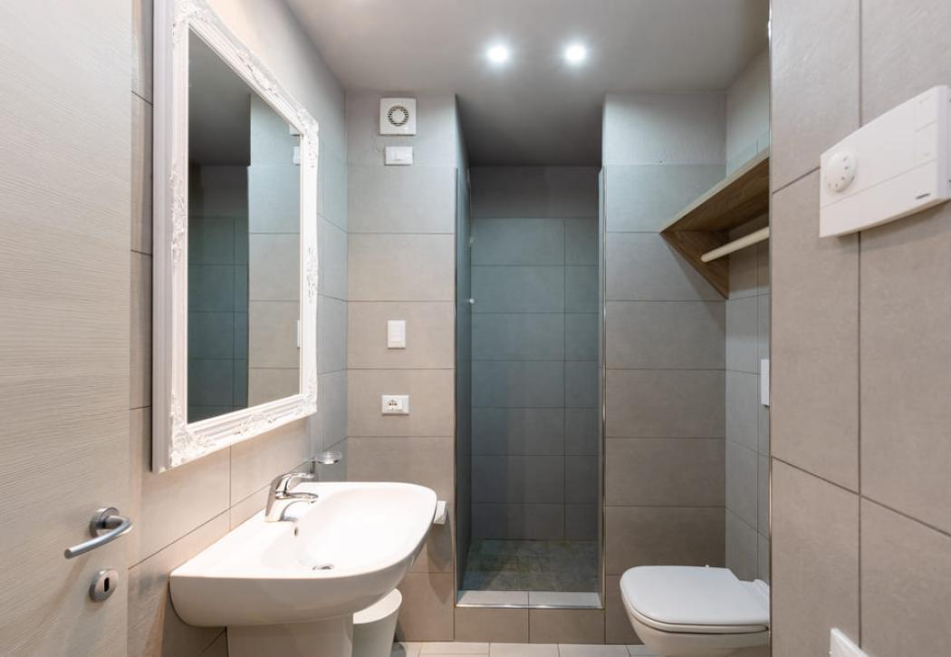 Bagno moderno con doccia, specchio decorato e lavabo bianco.
