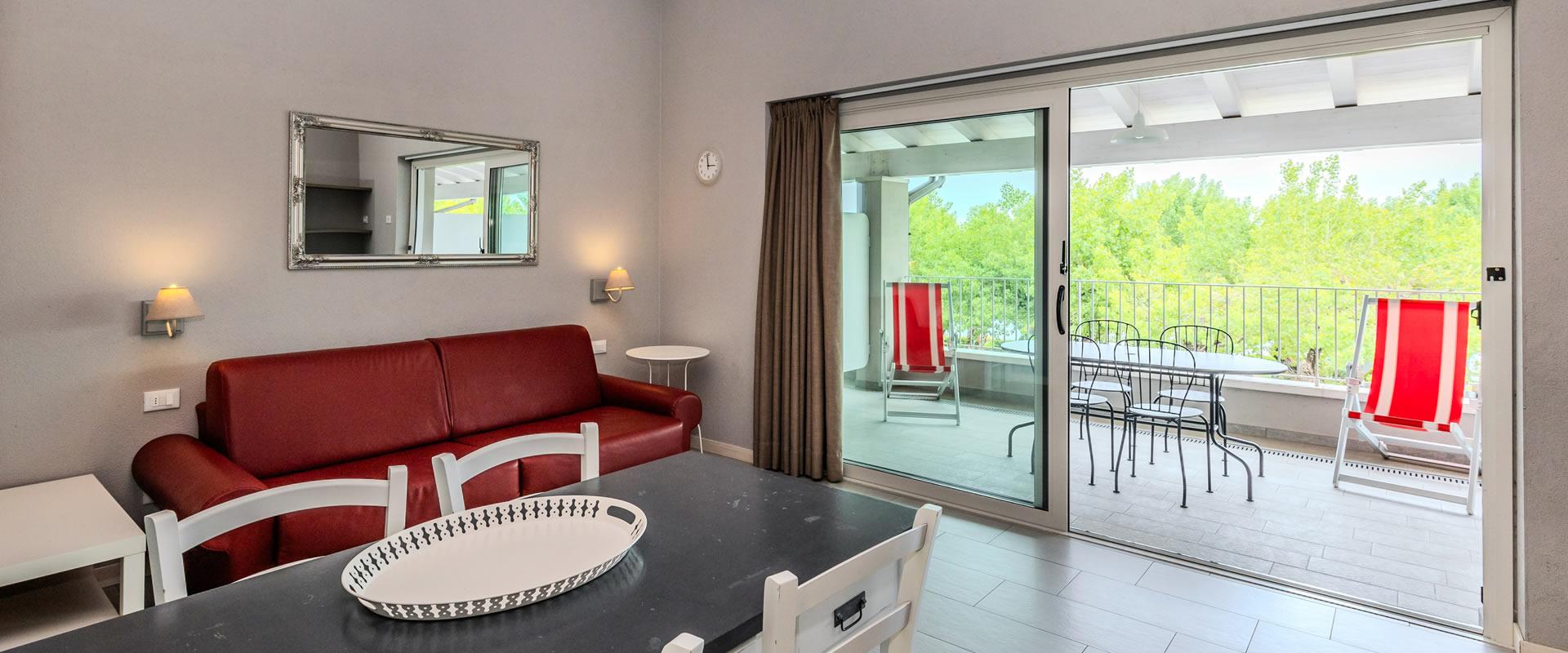 Soggiorno luminoso con divano rosso e balcone con vista verde.