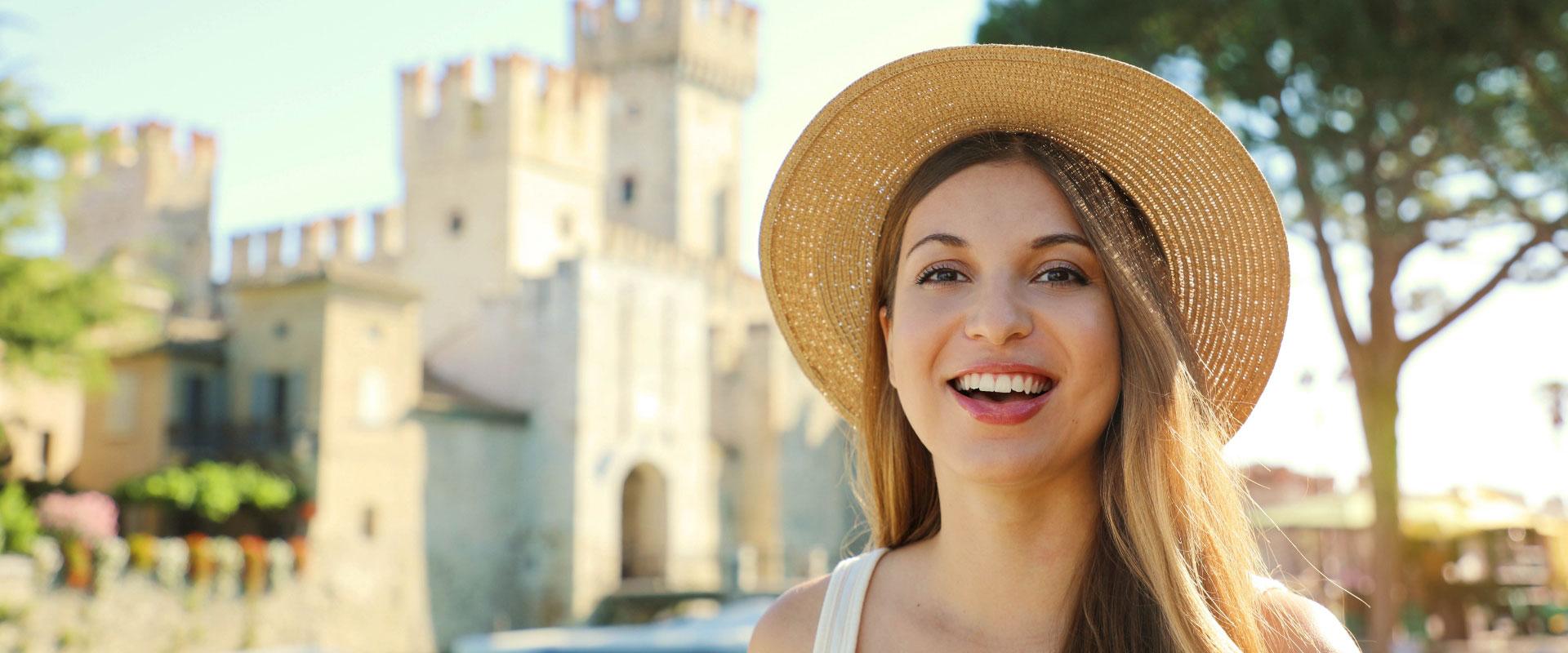 Donna sorridente con cappello di paglia davanti a un castello.