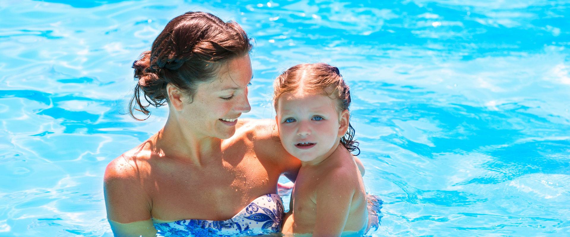 Mother and child swimming together in the pool, smiling.