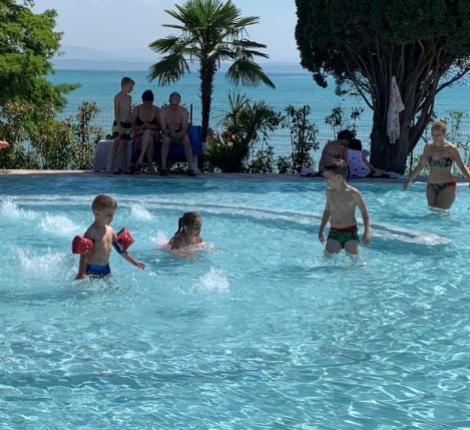 Des enfants jouent dans une piscine avec vue sur la mer par une journée ensoleillée.