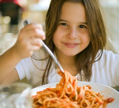 Lächelndes Mädchen isst Spaghetti mit Tomatensauce.