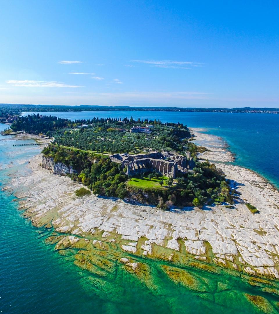 Vue aérienne d'une péninsule avec des ruines et une mer cristalline.